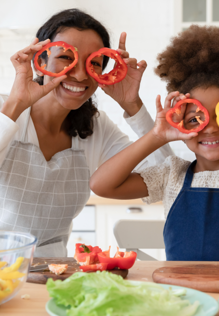 Nutritional Health Img Nutritional Health Img Alt Text: Young Mother and Daughter in the kitchen holding up sliced peppers to look through.
