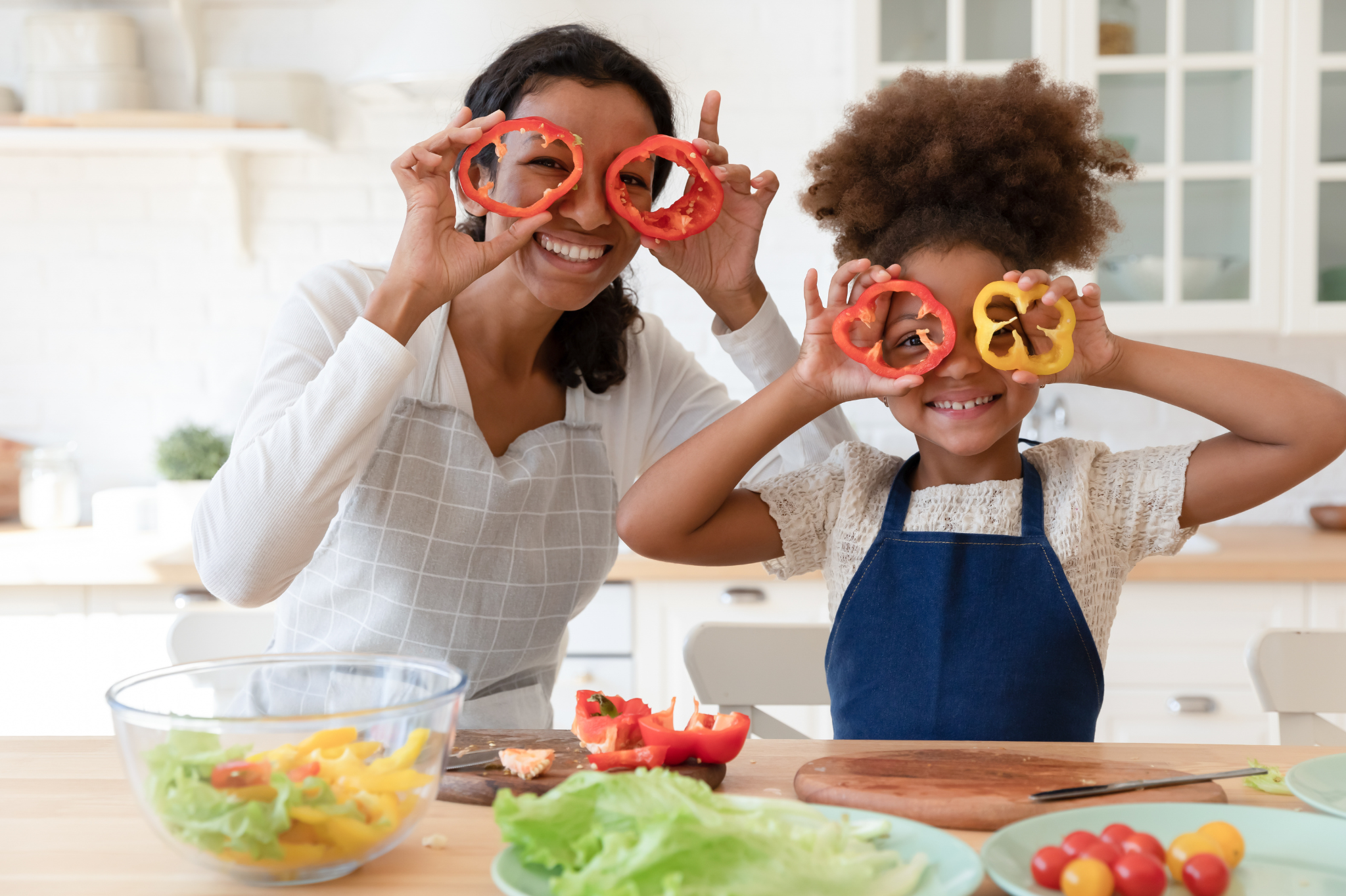 Nutritional Health Img Alt Text: Young Mother and Daughter in the kitchen holding up sliced peppers to look through.
